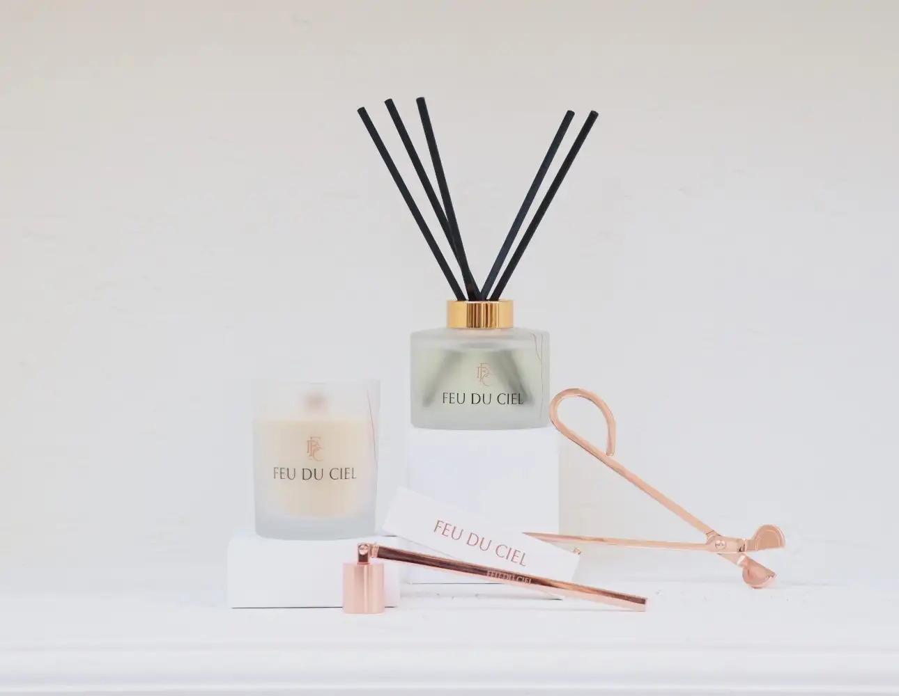 Feu du Ciel marka mum, oda kokusu ve mum söndürücü aksesuarları minimalist bir arka planda.